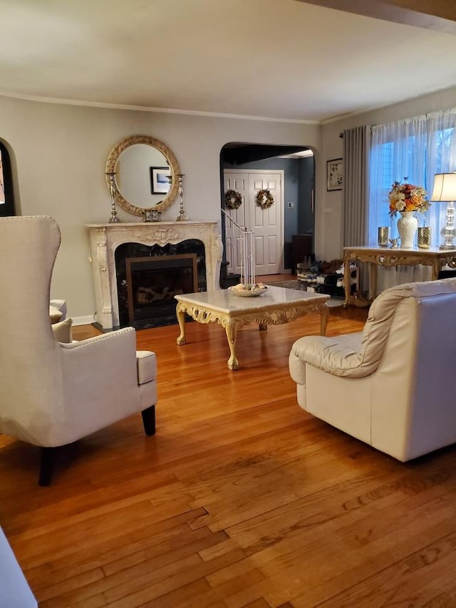 living room with crown molding, arched walkways, wood finished floors, and a high end fireplace
