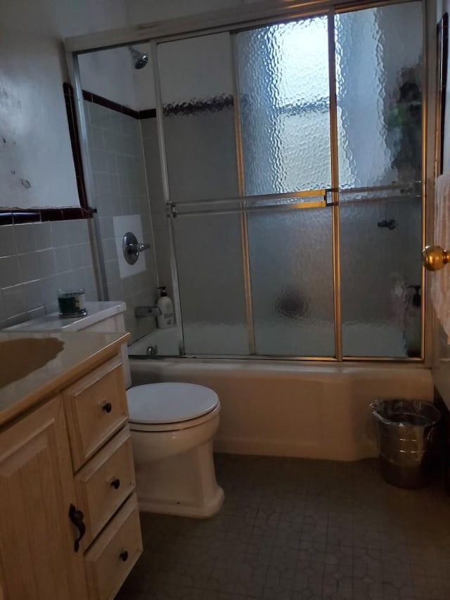 bathroom featuring toilet, tile walls, bath / shower combo with glass door, and vanity