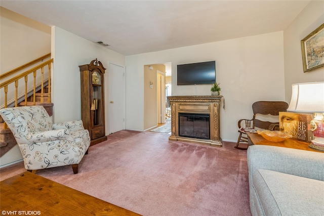carpeted living area with a glass covered fireplace, stairway, and visible vents