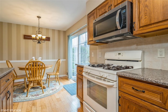 kitchen with stainless steel microwave, light wood-type flooring, a notable chandelier, white range with gas cooktop, and brown cabinetry