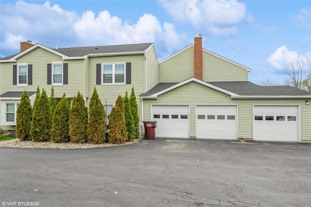 view of front of house featuring an attached garage, a shingled roof, a chimney, and aphalt driveway