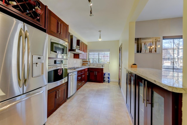 67-54 Groton St, Forest Hills, NY 11375 - kitchen with light stone counters, wall chimney range hood, reddish brown cabinets, a sink, and appliances with stainless steel finishes