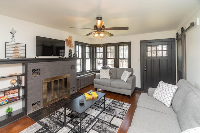 living area featuring radiator heating unit, a brick fireplace, wood finished floors, and a barn door