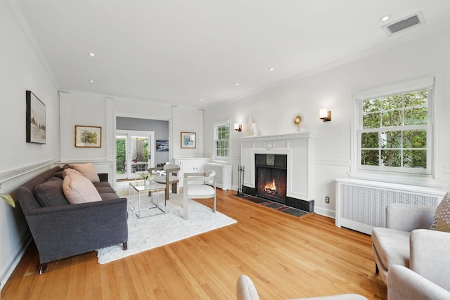 living area with radiator heating unit, ornamental molding, healthy amount of natural light, and wood finished floors
