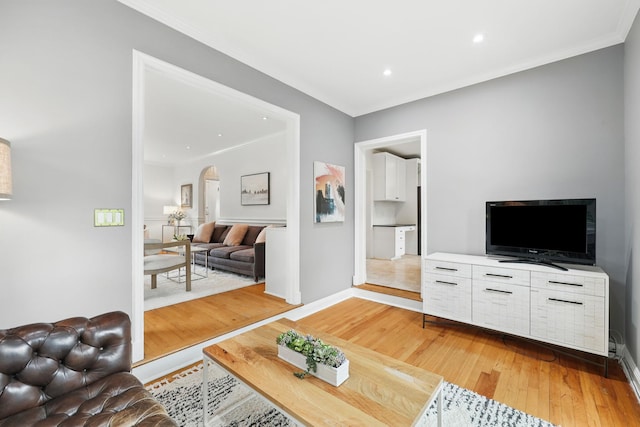 living room featuring arched walkways, light wood-style floors, crown molding, baseboards, and recessed lighting