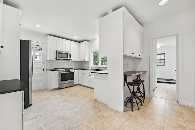 kitchen featuring appliances with stainless steel finishes, a baseboard radiator, dark countertops, white cabinetry, and recessed lighting