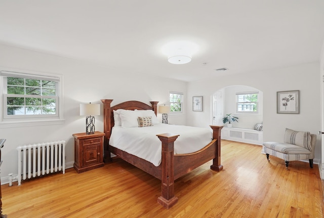 bedroom with radiator, multiple windows, light wood-type flooring, and arched walkways
