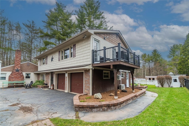 view of home's exterior featuring stone siding, a garage, a lawn, a balcony, and aphalt driveway
