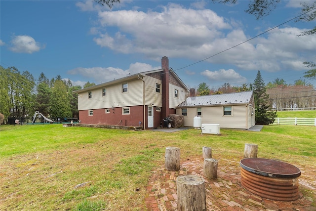 back of house with a chimney, fence, a fire pit, and a lawn