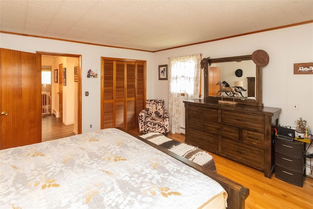 bedroom featuring a baseboard heating unit, light wood-style floors, a closet, and crown molding