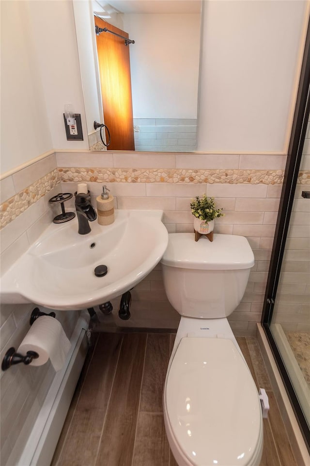 bathroom featuring a shower stall, a sink, tile walls, a wainscoted wall, and toilet