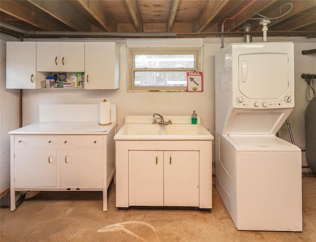 laundry room featuring cabinet space, stacked washing maching and dryer, and a sink