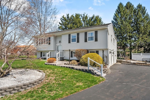 bi-level home featuring fence, aphalt driveway, a front yard, and a garage