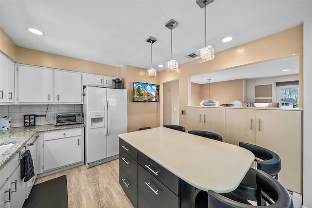 kitchen featuring white cabinets, a kitchen breakfast bar, visible vents, pendant lighting, and white refrigerator with ice dispenser