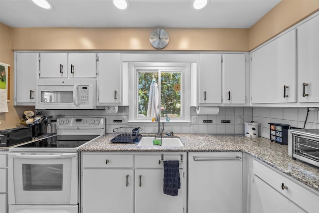 kitchen with a sink, white appliances, light stone countertops, decorative backsplash, and white cabinetry