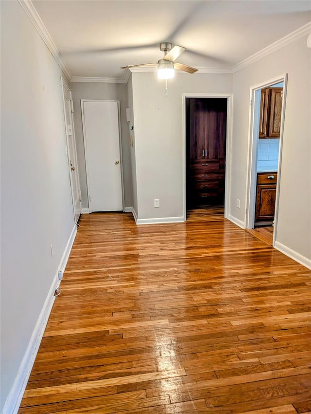 unfurnished bedroom with crown molding, ceiling fan, baseboards, wood-type flooring, and ensuite bath
