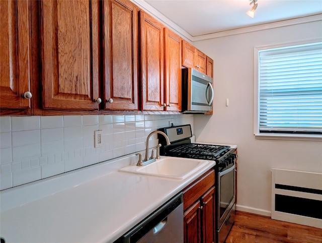 kitchen with light countertops, wood finished floors, a sink, tasteful backsplash, and appliances with stainless steel finishes