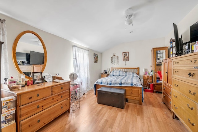 bedroom featuring light wood finished floors, vaulted ceiling, a fireplace, and a ceiling fan