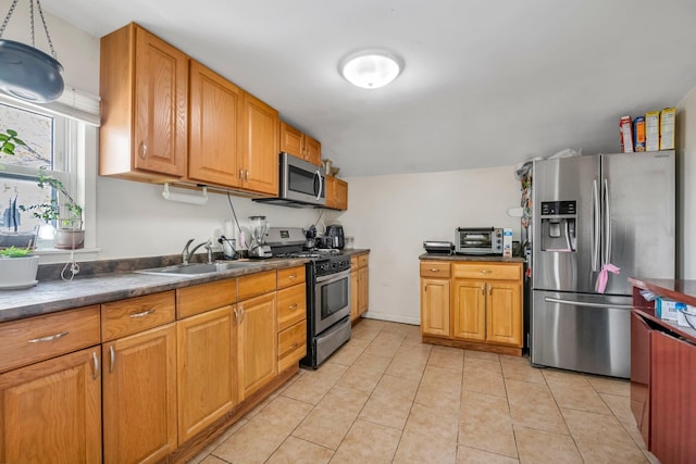 kitchen with dark countertops, a sink, brown cabinets, light tile patterned floors, and stainless steel appliances