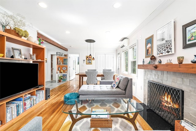 living area with a wall mounted air conditioner, wood finished floors, a tiled fireplace, ornamental molding, and recessed lighting