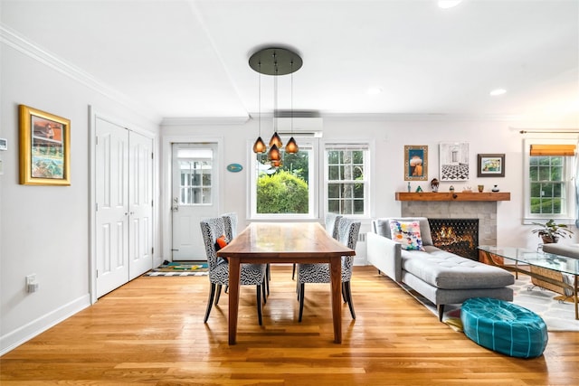 dining room featuring light wood finished floors, a wall mounted AC, crown molding, and a warm lit fireplace