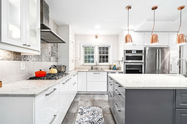 kitchen with gray cabinetry, a sink, appliances with stainless steel finishes, and wall chimney range hood