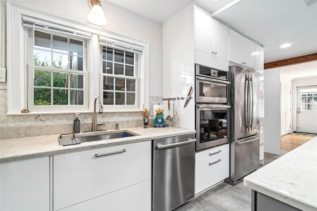 kitchen with white cabinets, a sink, decorative backsplash, light wood-style flooring, and appliances with stainless steel finishes