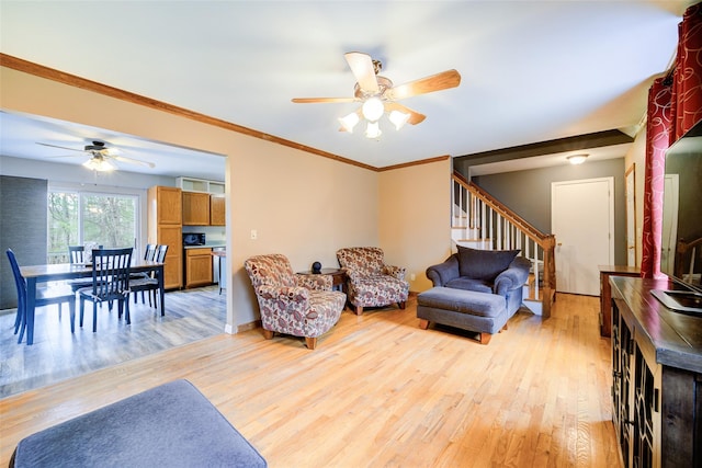 living area featuring stairs, light wood-type flooring, ceiling fan, baseboards, and ornamental molding