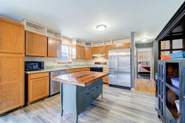 kitchen featuring light wood-style flooring, a sink, butcher block counters, under cabinet range hood, and appliances with stainless steel finishes