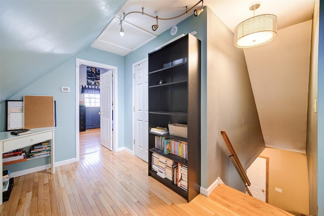 hall featuring hardwood / wood-style floors, baseboards, an upstairs landing, and lofted ceiling