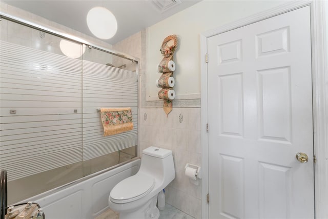 full bath featuring bath / shower combo with glass door, toilet, tile walls, wainscoting, and visible vents