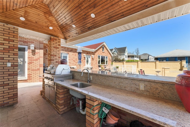 view of patio / terrace with an outdoor kitchen, a sink, fence, a residential view, and grilling area