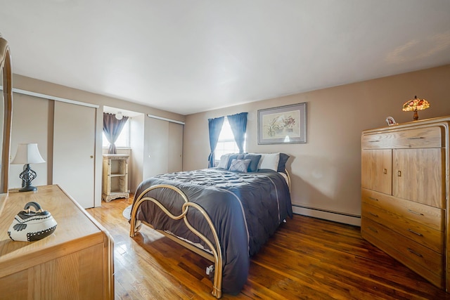 bedroom featuring a baseboard heating unit, two closets, wood-type flooring, and multiple windows