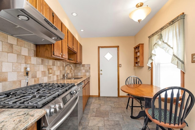 kitchen featuring stainless steel range with gas stovetop, a sink, decorative backsplash, brown cabinetry, and under cabinet range hood