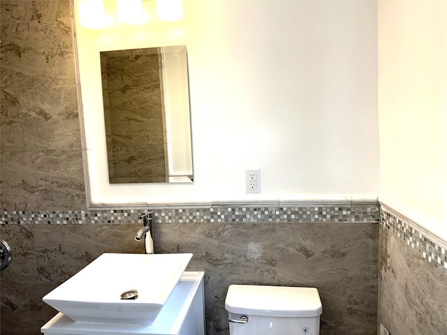 half bath featuring toilet, tile walls, wainscoting, and vanity