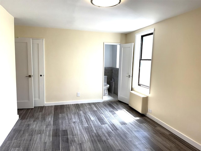 empty room featuring dark wood-style flooring, baseboards, and radiator