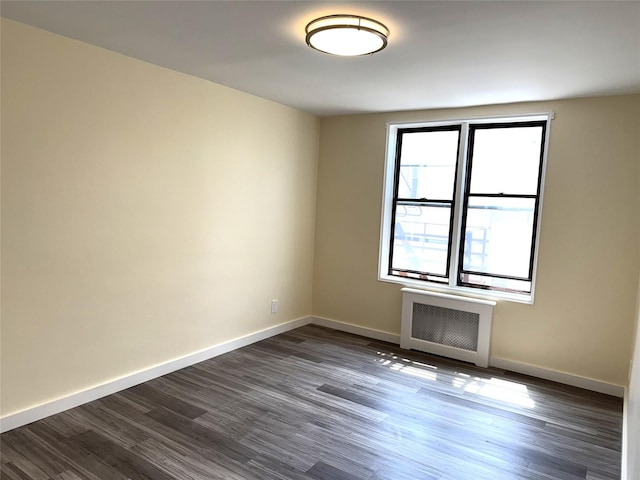 spare room featuring dark wood-style flooring, baseboards, and radiator heating unit