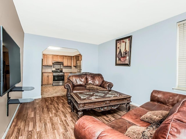 living area featuring arched walkways, baseboards, and dark wood-style floors