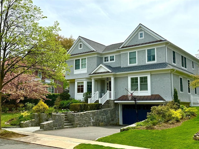 shingle-style home with a garage, aphalt driveway, a front yard, roof with shingles, and a standing seam roof