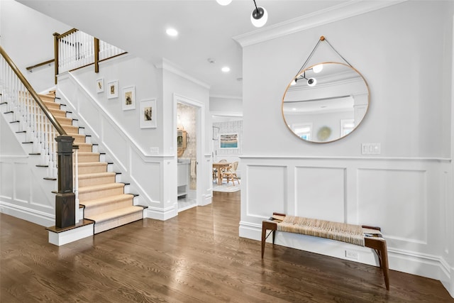 foyer featuring a decorative wall, a wainscoted wall, wood finished floors, stairway, and crown molding