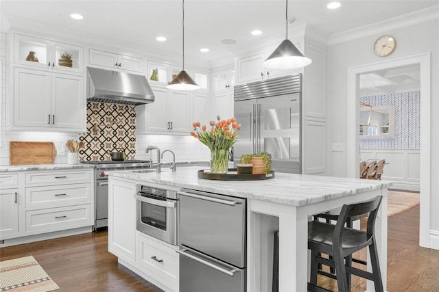 kitchen featuring a kitchen bar, a sink, stainless steel appliances, white cabinetry, and under cabinet range hood