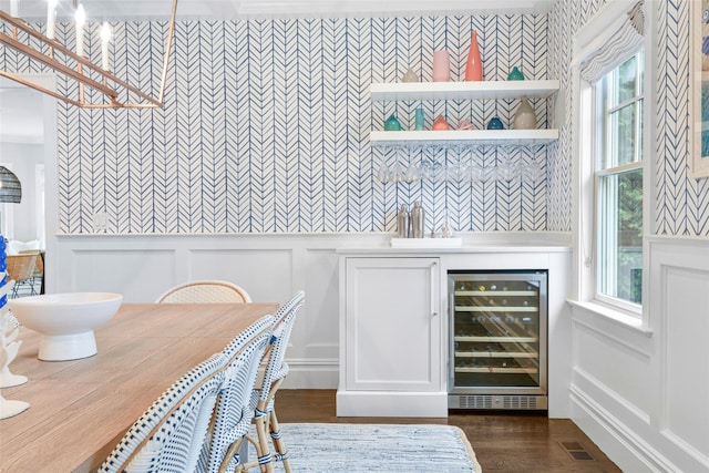 dining area featuring a decorative wall, wine cooler, wainscoting, a community bar, and wallpapered walls
