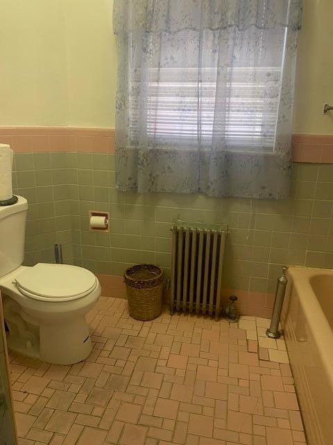 full bath featuring a bathtub, tile walls, a wainscoted wall, toilet, and radiator