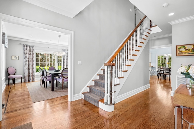 stairs featuring crown molding, wood finished floors, a notable chandelier, and a wealth of natural light