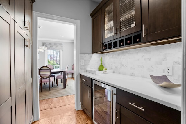 bar with light wood-style floors, beverage cooler, tasteful backsplash, ornamental molding, and a bar