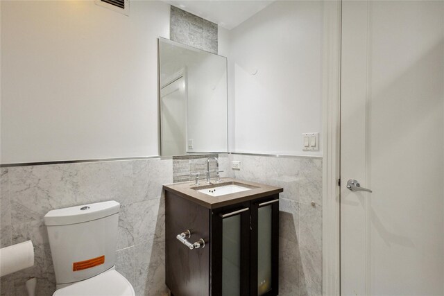 bathroom with vanity, toilet, a wainscoted wall, tile walls, and visible vents