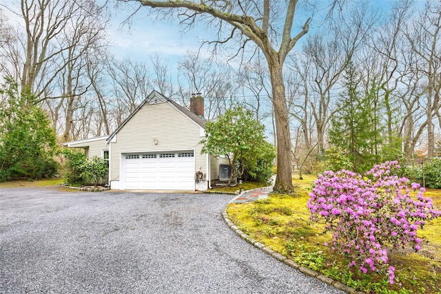 view of property exterior with a chimney, an attached garage, and driveway