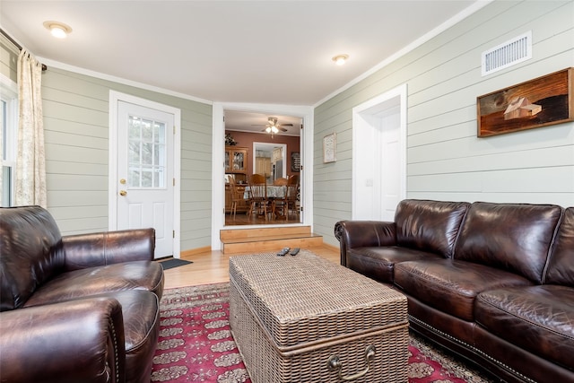 living area featuring visible vents, crown molding, wood finished floors, and wooden walls