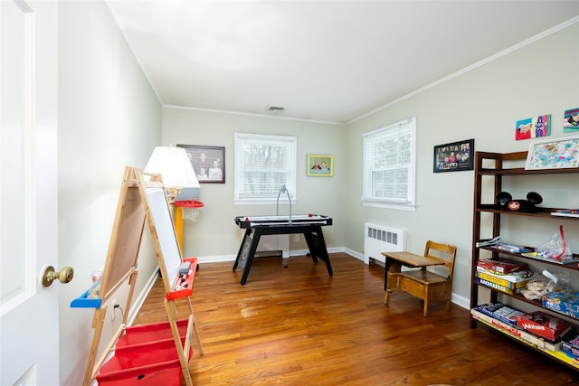 playroom featuring visible vents, wood finished floors, baseboards, radiator heating unit, and ornamental molding