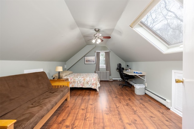 bedroom with vaulted ceiling with skylight, baseboard heating, a ceiling fan, and wood finished floors